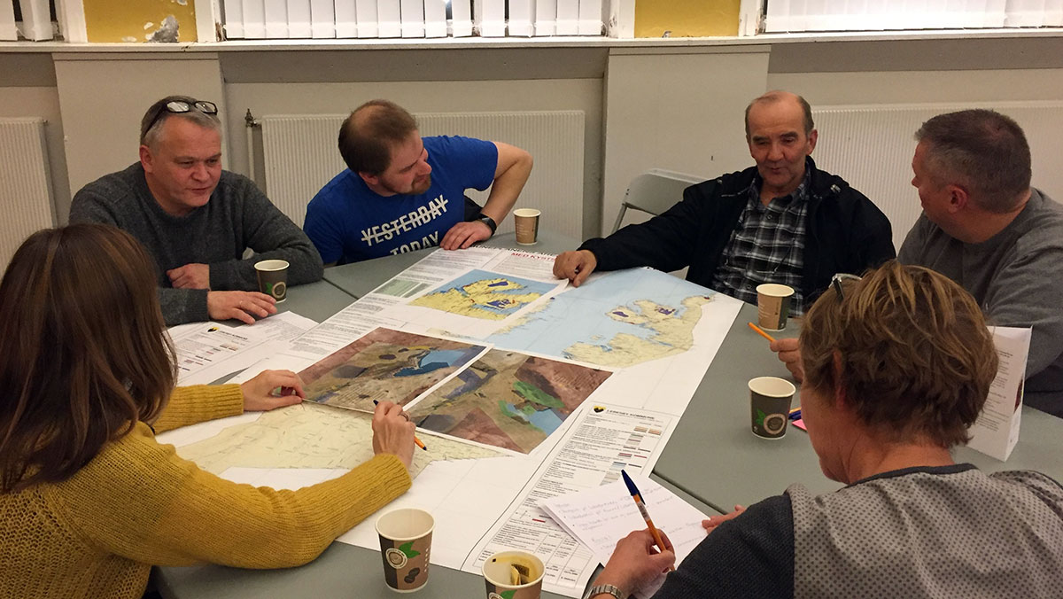 6 personer samlet rundt et bord med kart og planer på. Foto.