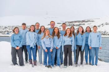 Gruppebilde av 16 ungdommer som står foran en elv. Bakken er dekket med snø og vi ser noen hvite fjell bak elven de står ved.