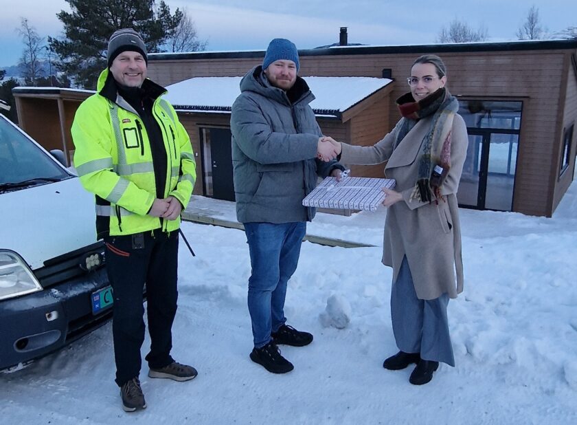 Tre personer står foran et hus. Det er vinter. De to personene til høyre tar hverandre i hånden som om at de inngår en avtale.