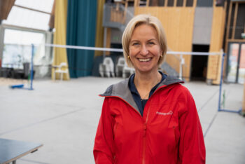 En kvinne i rød jakke står foran et volleyballnett